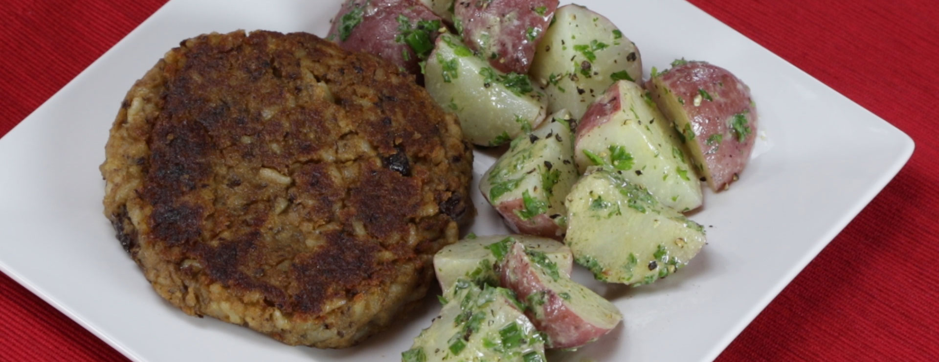 a plate with a black bean burger patty next to some potato salad