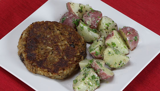 a plate with a black bean burger patty next to some potato salad