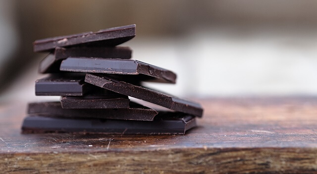 Broken pieces of dark chocolate are stacked on a table.