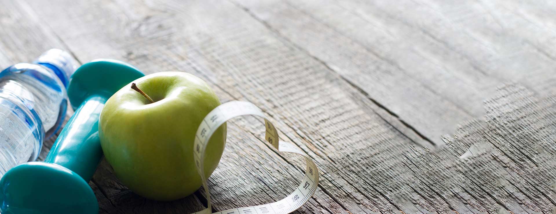 An apple, weights, and water bottle arranged on the floor