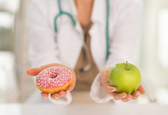 A doctor holds a donut in one hand and an apple in the other.