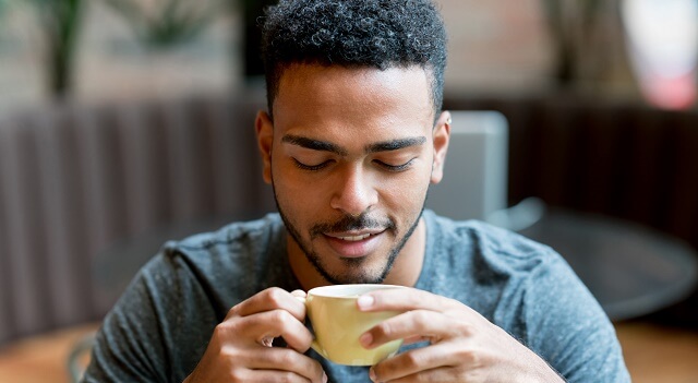 A young man drinks a cup of coffee in a cafe.