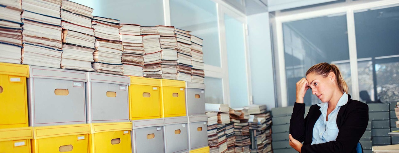Woman stressed at work looking at a shelf full of files