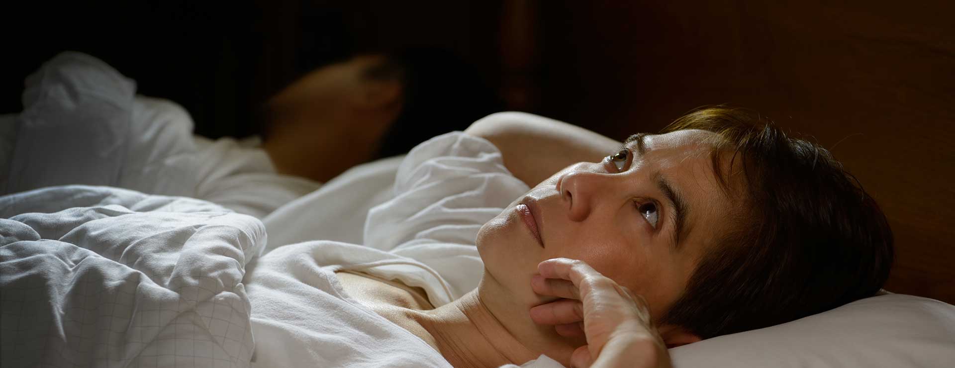 A woman lies awake in bed looking at ceiling