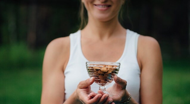 A woman holds a cup of nuts outside.