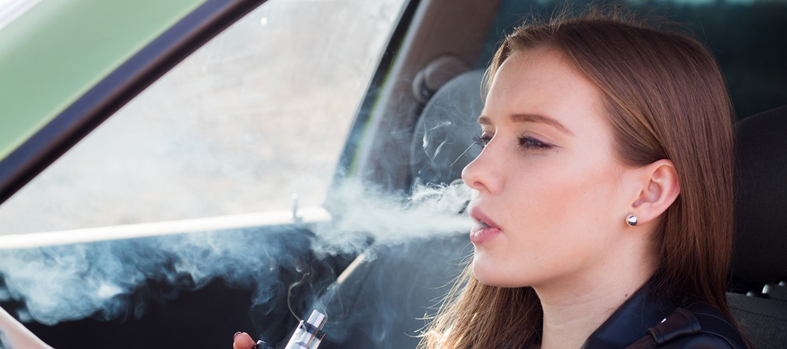 A woman exhales a cloud of vapor in her car.