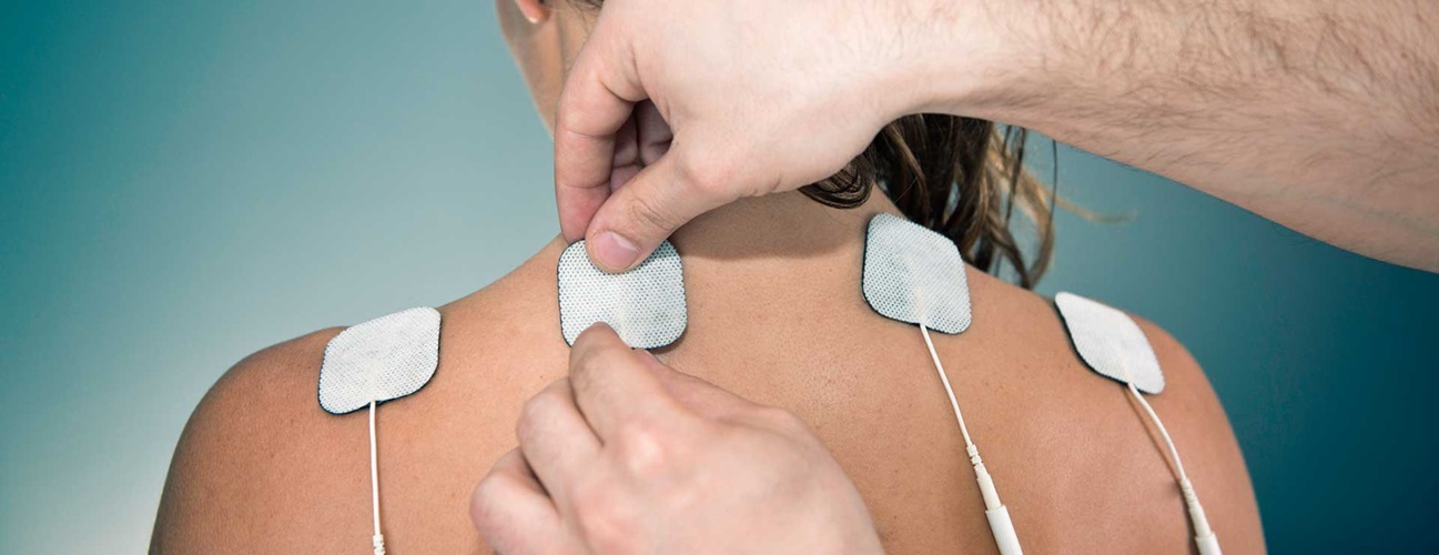 A practitioner applies electrodes to a woman's back.