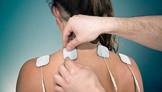 A practitioner applies electrodes to a woman's back.