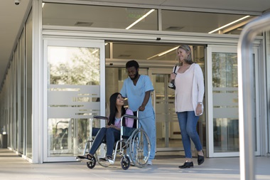 Young patient in a wheelchair leaving a hospital with their parent