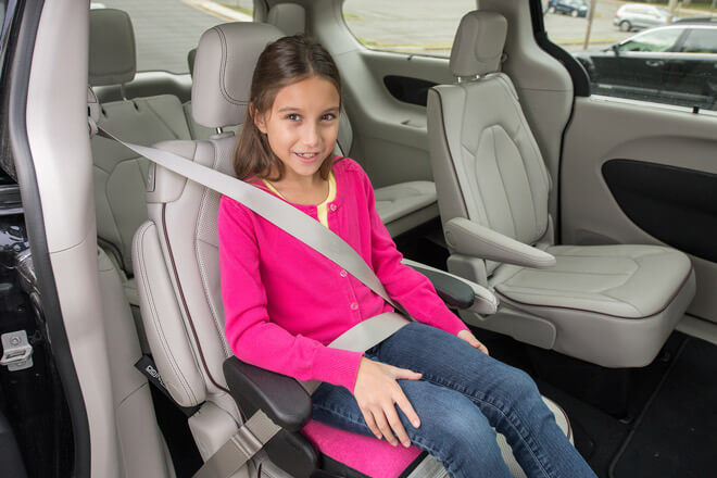 A young child sits in a booster seat in the back of a vehicle