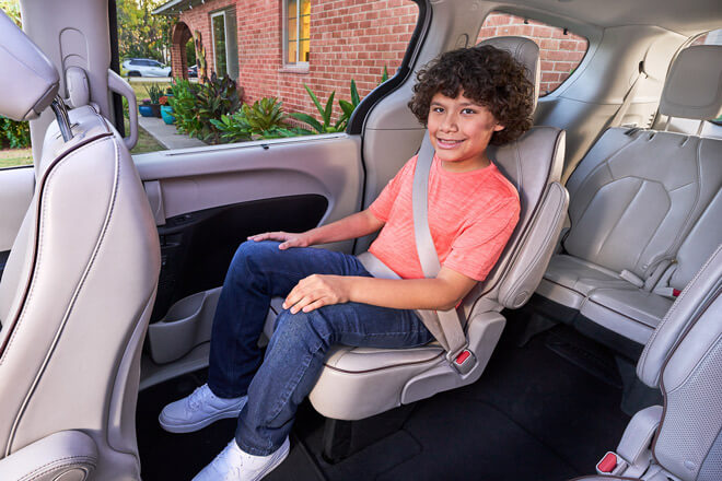 An older child sits in the back of a car wearing a seat belt
