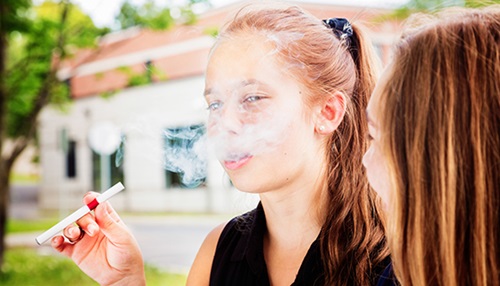 A young girl exhales from a vape pen.