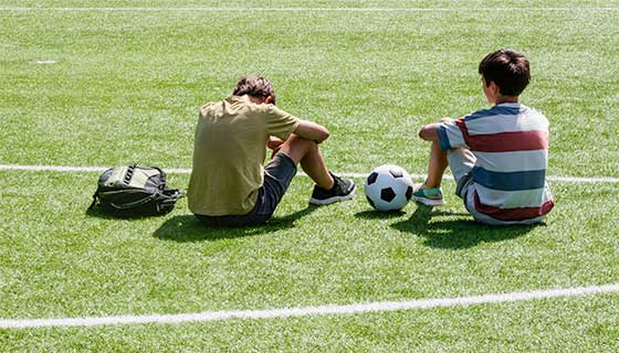 Two student athletes sitting on a soccer field, one with their head held low.