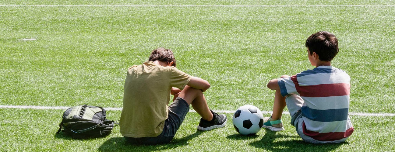 Two student athletes sitting on a soccer field, one with their head held low.