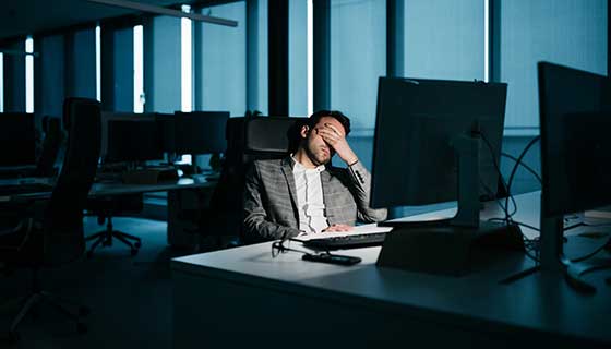 Mans rubs his eyes in frustration as he sits in a dark office
