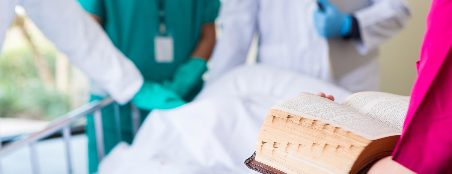 Healthcare providers reading religious texts over patient bed