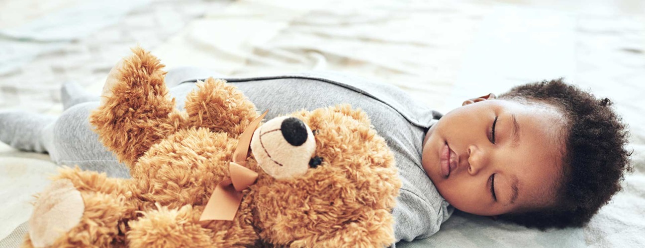 a baby sleeps in bed with teddy bear