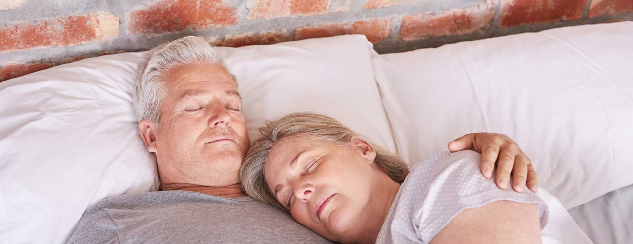 A senior man sleeps in bed with wife
