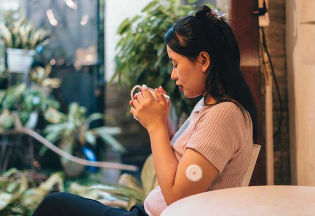 Woman with continuous glucose monitoring device drinking tea
