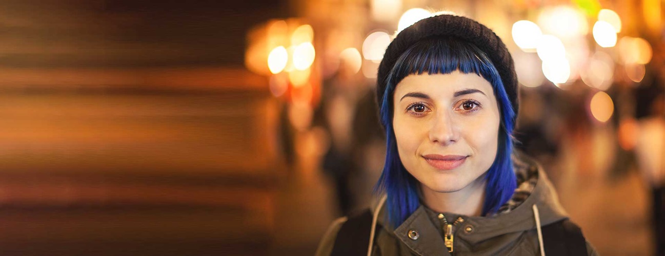 A blue-haired millennial woman looks directly at the camera, smiling slightly.