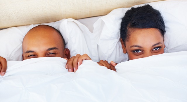 Couple peeking out from under sheets