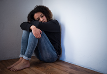 A young black woman sits on the floor, looking sad.