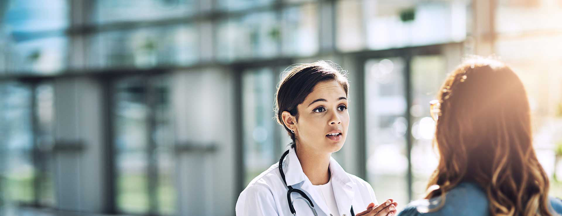 Woman speaking with doctor in sunny lobby