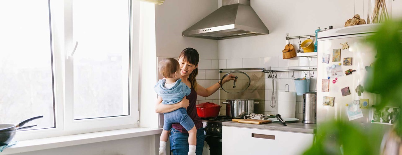 A mother holds her baby while cooking.