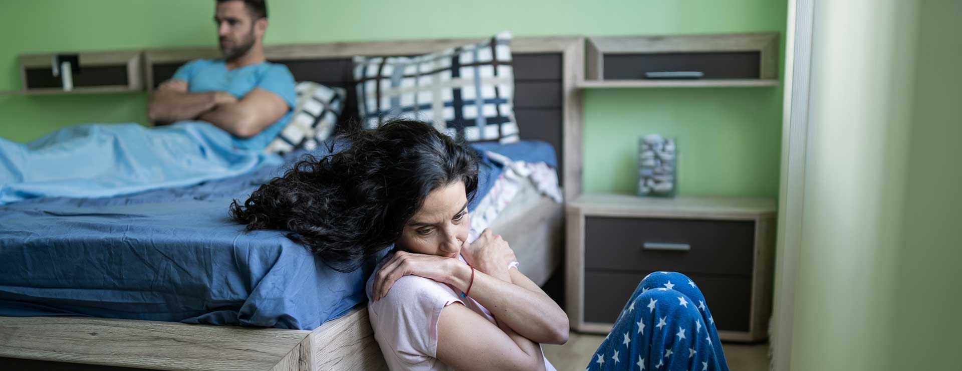 Upset woman sitting on the floor leaning against her bed