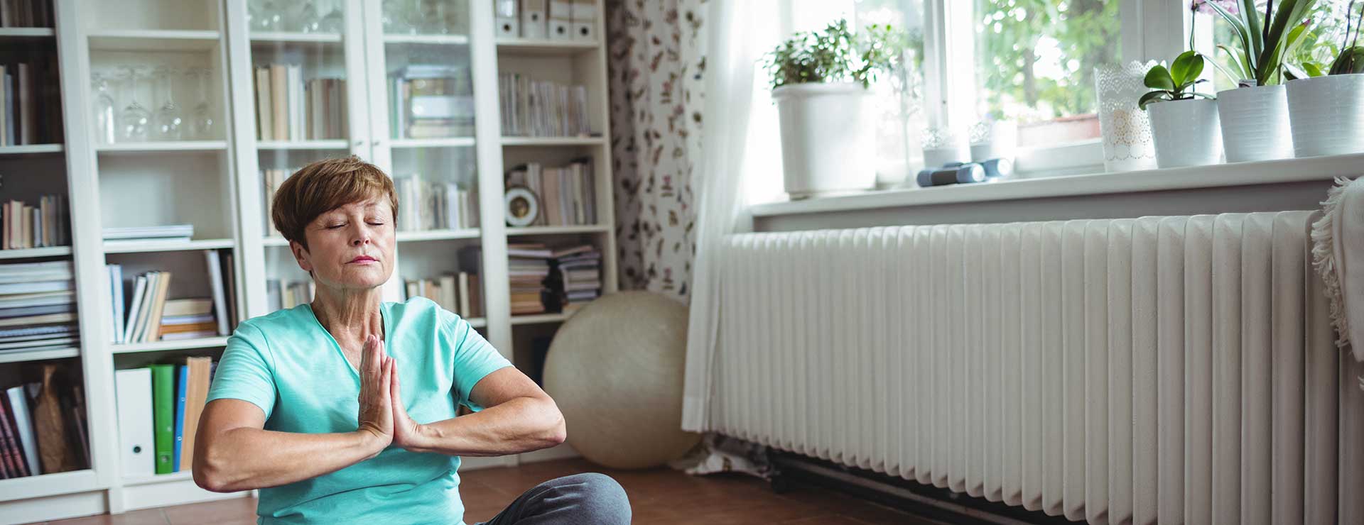 A senior woman sits on the floor, meditating.