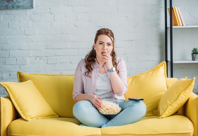 A woman sits on the couch, eating popcorn.