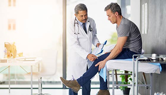 Doctor examines a man's knee in a sunny exam room