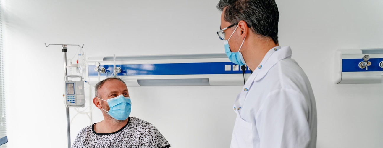Masked man talks with masked doctor.