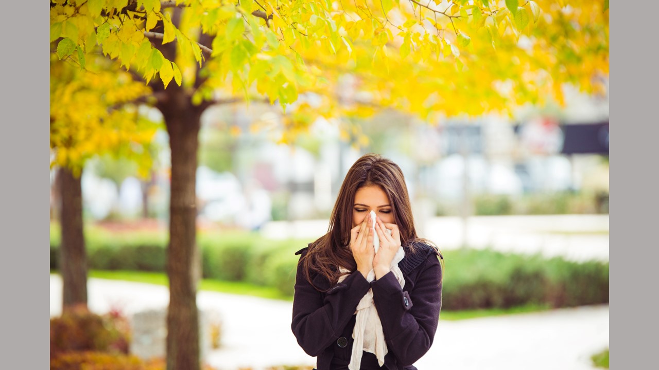 woman blowing nose in front of yellow trees