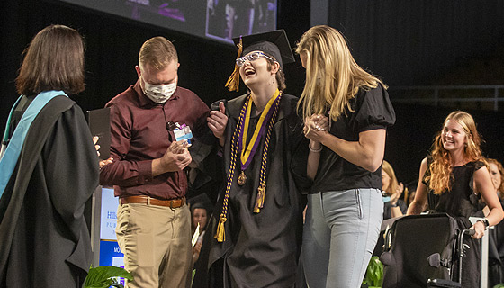 Hailey walking at graduation with the help of her physical therapists. 