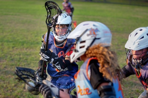 James, a young boy, playing lacrosse in a field with his teammates. 