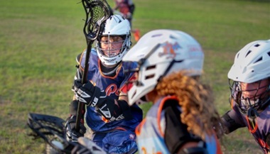 James, a young boy, playing lacrosse in a field with his teammates. 