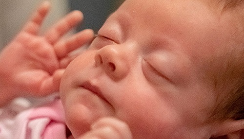 Newborn baby with their eyes closed and hands by their face.