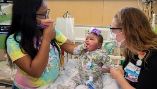Malani, a baby girl about one year old, receives care from a nurse at Johns Hopkins All Children's Hospital in St. Petersburg, Florida. Her mother stands next to the hospital bed.