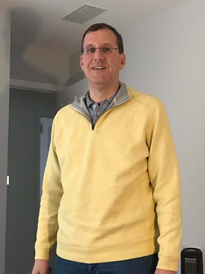 Mike stands in home wearing yellow sweater