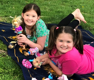 Morgan and sister Natalie playing with dolls in the grass