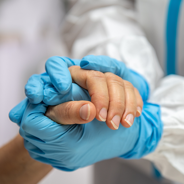 A photo shows a healthcare worker's hands holding a patient's hands.  