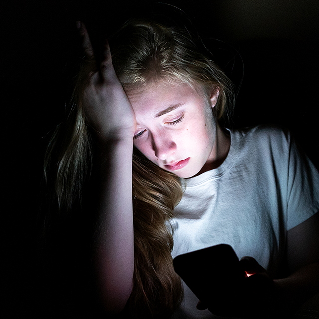 A photo shows an adolescent sitting and grasping her forehead.