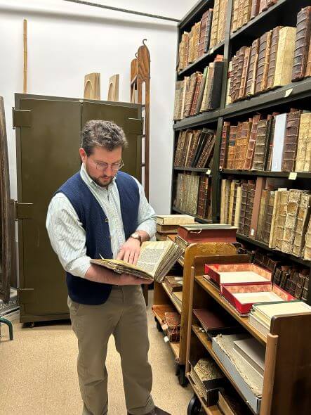 Photo of Michael Seminara standing in front of a shelf of ancient manuscripts