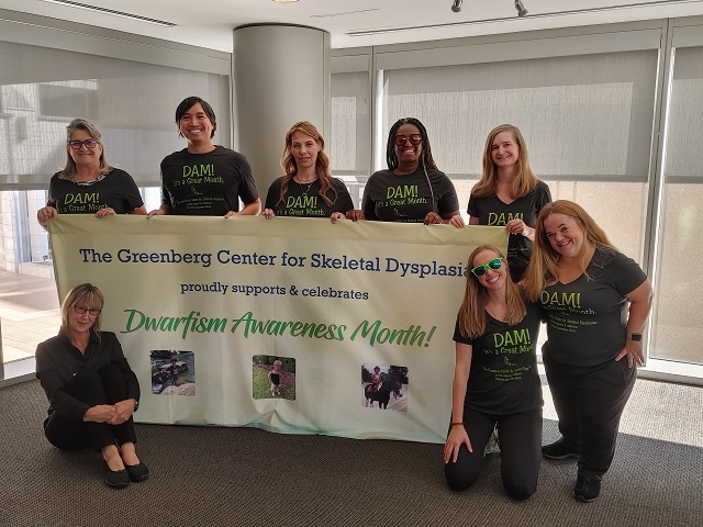 Members of the Greenberg Center team holding a dwarfism awareness banner.