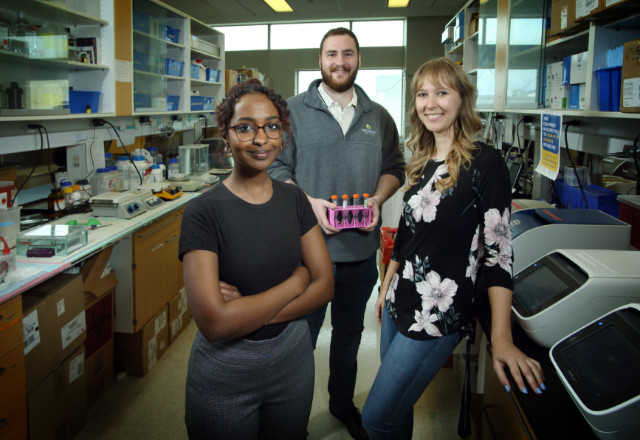 3 predoctoral human genetics students standing between 2 lab benches