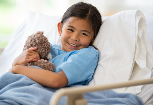 Girl in hospital bed cuddling a teddy bear