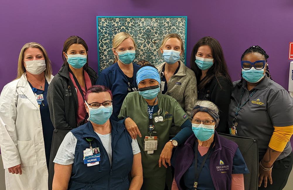 Masked pediatric team group photo, in front of a purple wall.