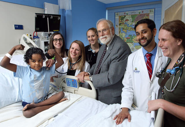 George Dover, director of the Department of Pediatrics, with residents and boy in hospital bed, flexing muscles