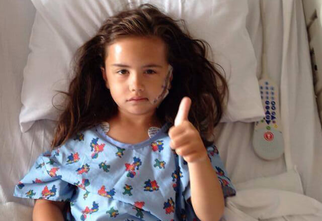 Demi sits in her hospital bed and gives a thumbs up